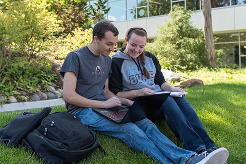 Students sitting outside looking at a laptop.