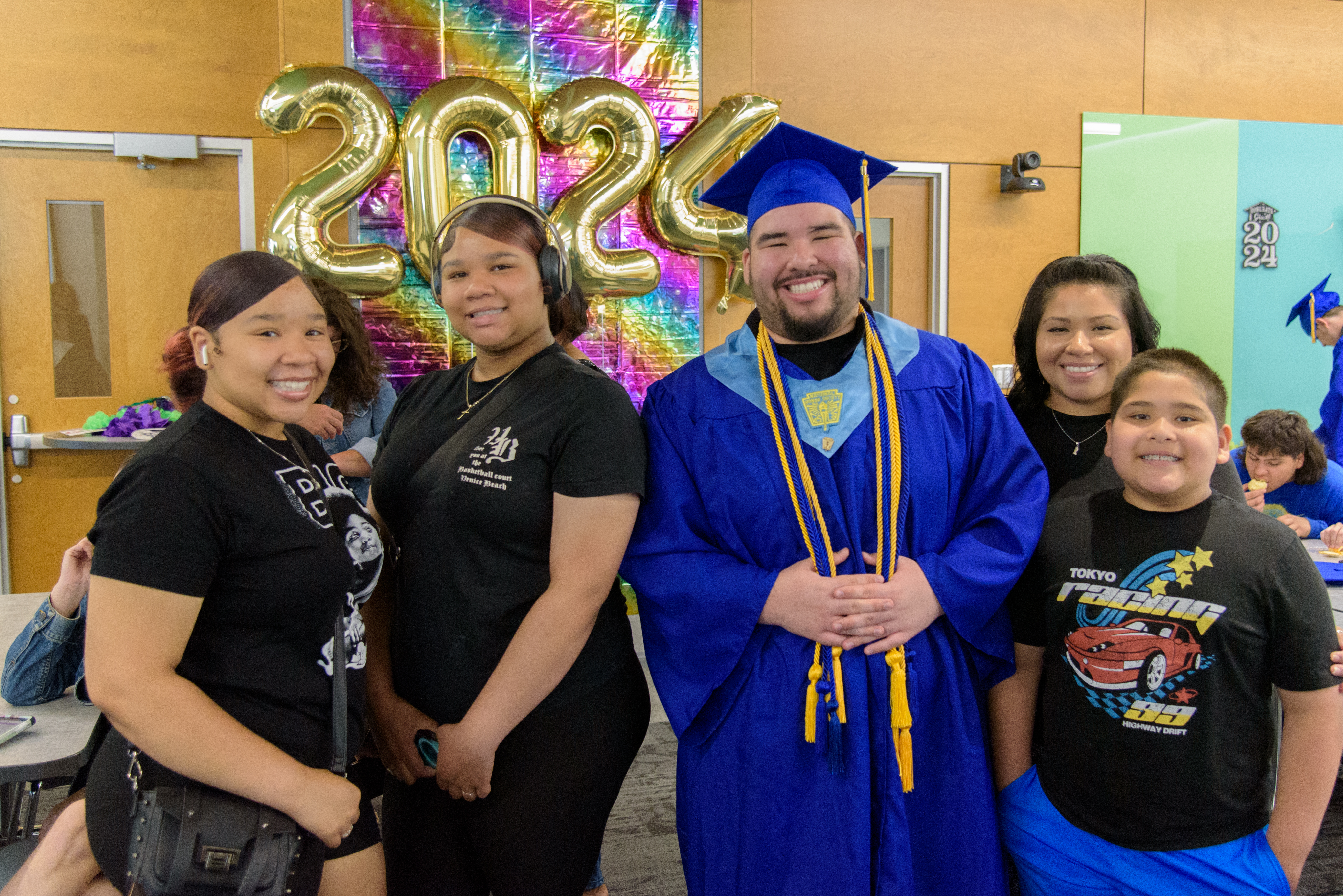 Eli'sha Thomas wearing a blue cap and gown poses with his family in front of gold 2024 balloons