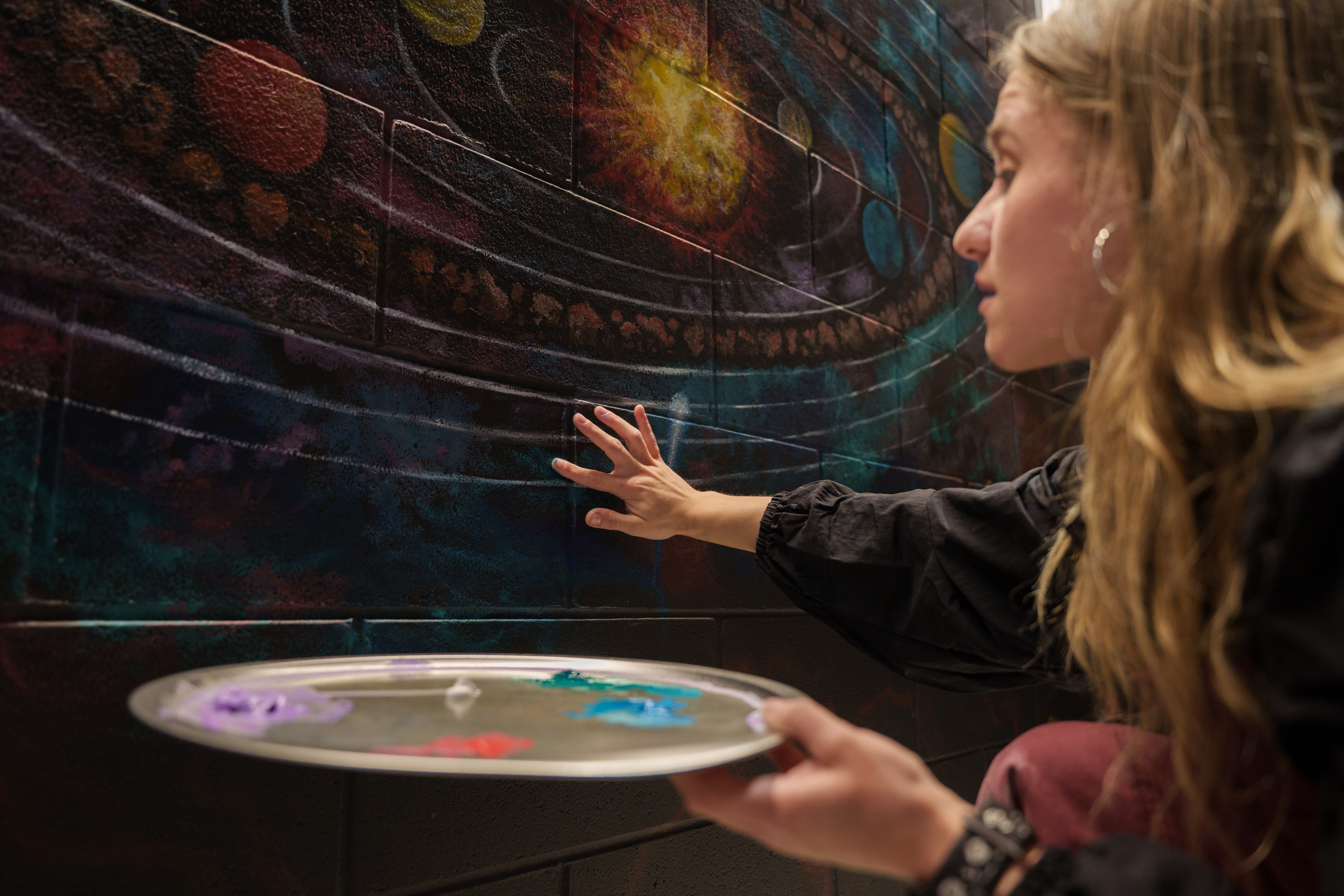 Morgan King finger painting the Delta College Delta Dome interior wall with a depiction of the solar system