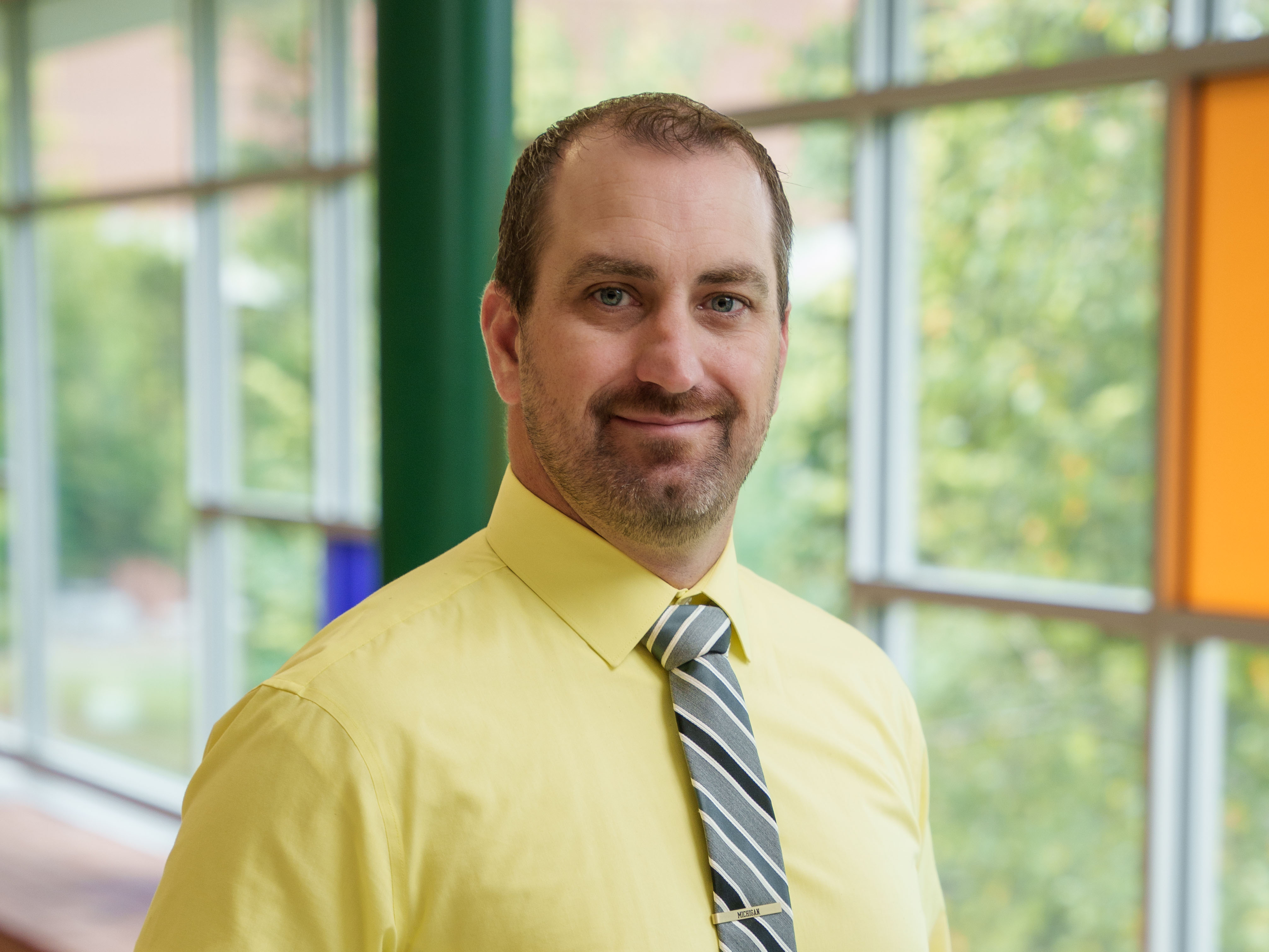 Jon Foco vice president of Business and Finance Jon Foco wearing yellow button-up shirt and blue striped tie, smiling for a photo